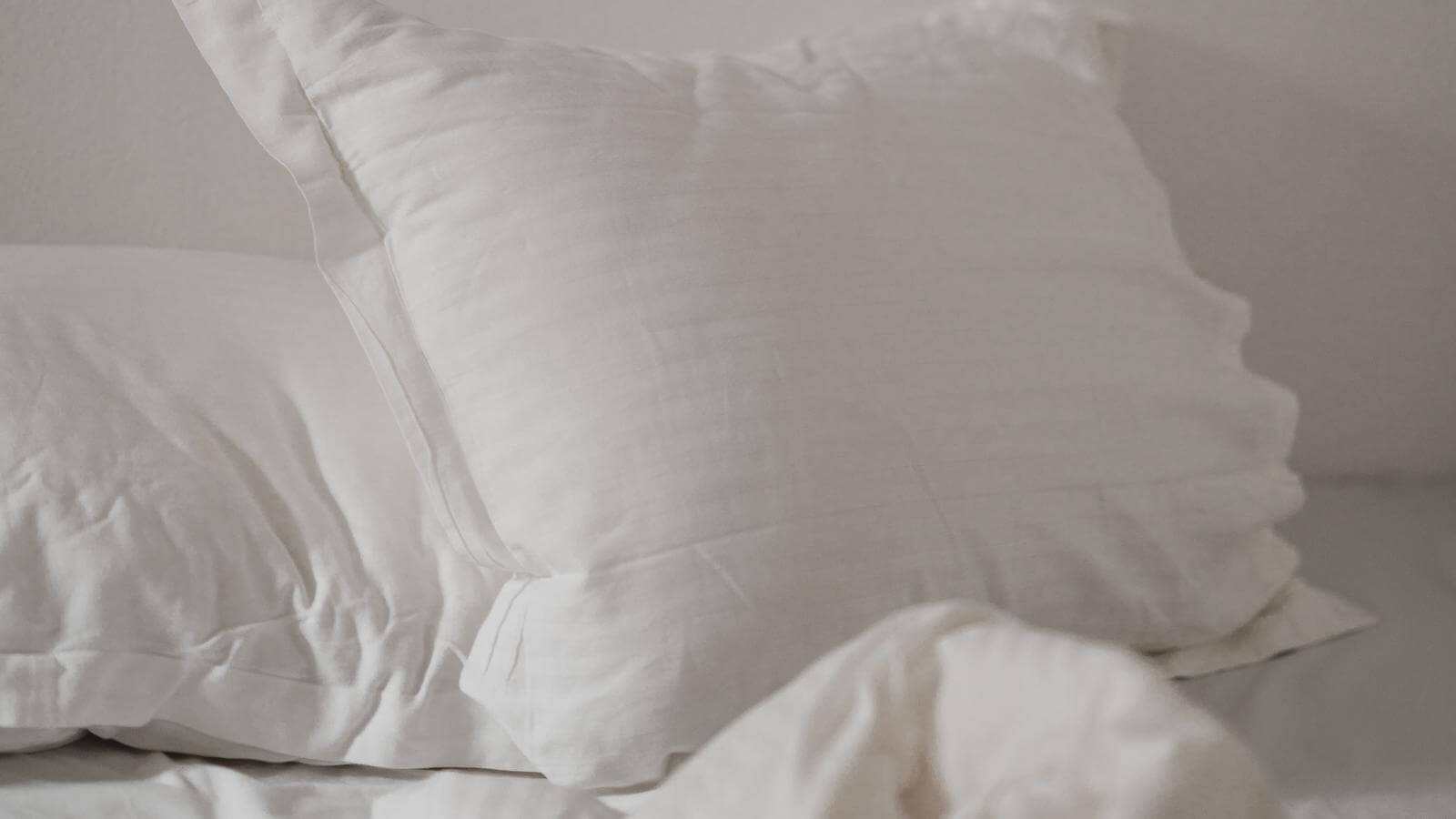 White pillow and sheets on a bed against a shite wall.