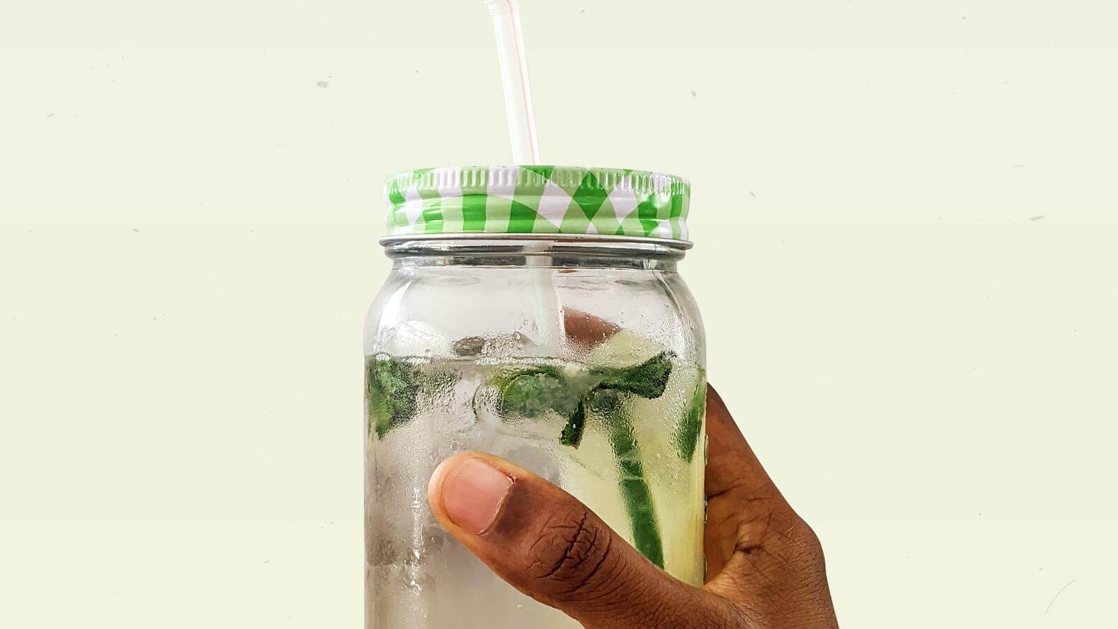 Glass of water infused with mint and cucumber, with a lid and straw.