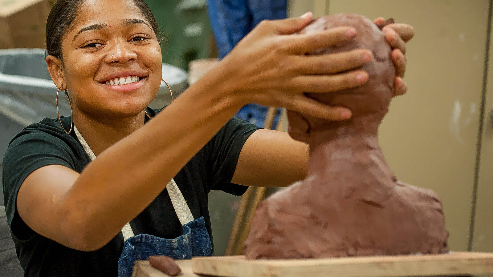 A student creating a clay bust sculpture.