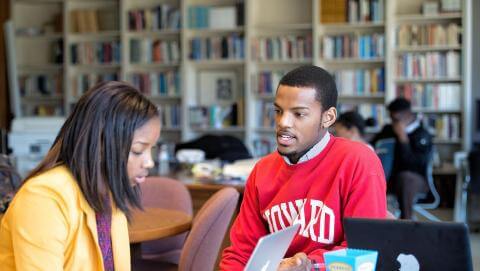 A woman in a yellow shirt and a men in a red Howard shirt studying together.