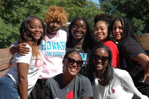 A group of seven Howard women huddled together, smiling in the sunshine.