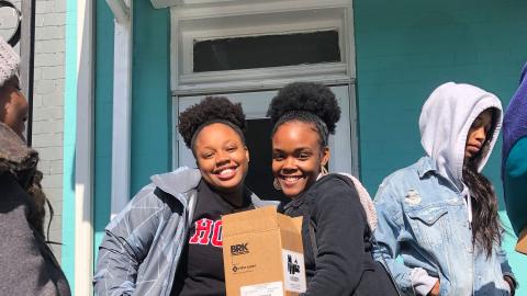 Two students smiling and holding a box on a front porch.