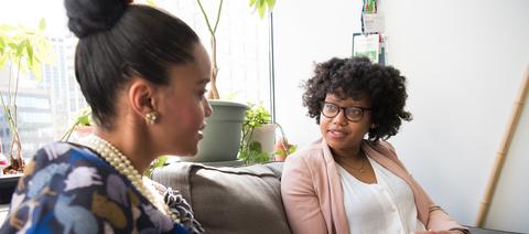 Two women sitting on a couch and talking together.