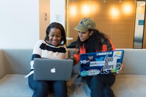 Two women sitting on a couch and using laptop computers.