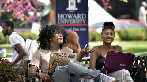 Two students on a bench together, using laptops.